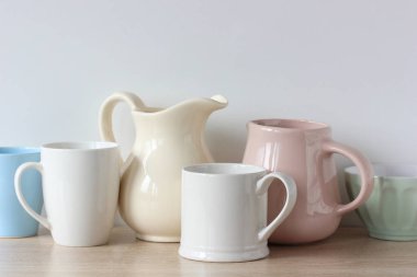 Tabaklar masaya yakın çekim. Rafta açık renkli sürahiler ve kupalar.