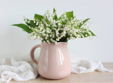 Masanın üzerinde pembe bir sürahi içinde vadideki orman zambakları. Bir buket beyaz çiçek. ışık bileşimi.