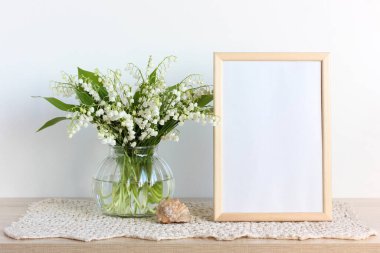 Vadi zambakları ve masanın üzerinde boş bir çerçeve. bahar ışığı arkaplanı, metin için boşluk.