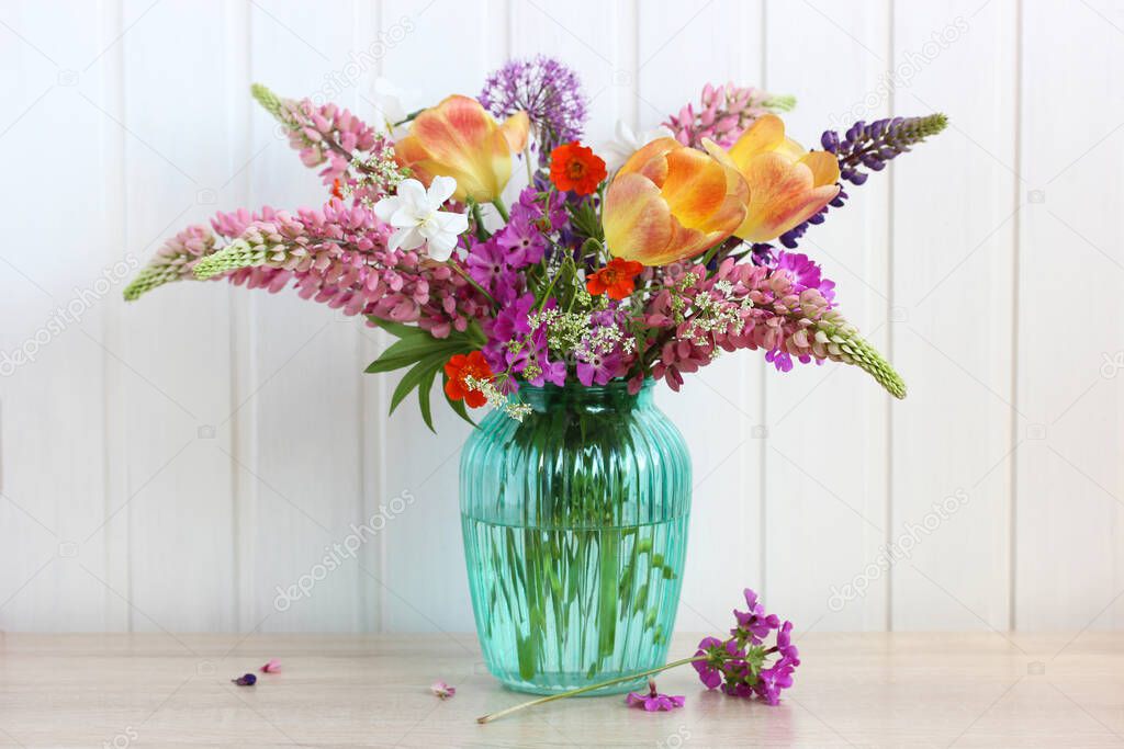 bright bouquet of flowers in a glass vase on the table. lupines, tulips, daffodils and other garden and wild flowers.