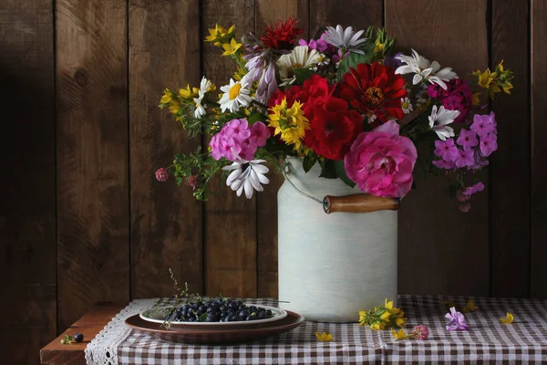 静谧的生活 有一束花园的花和蓝莓 放在桌子上的盘子里 靠着木墙 夏村的组成 — 图库照片