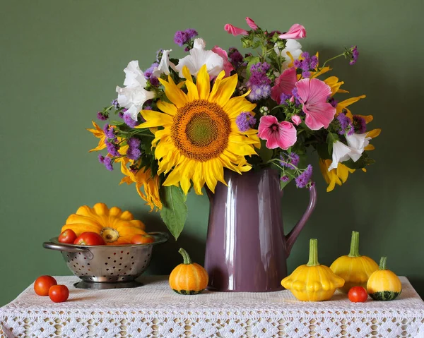 bouquet of garden flowers sunflower ageratum lavatera in a jug yellow pumpkins squash red tomatoes on the table a summer rustic still life with flowers and vegetables on a green background