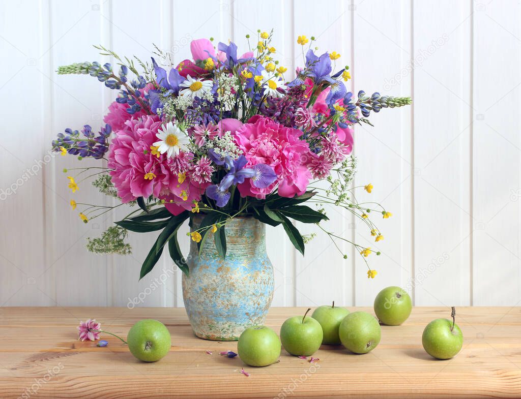bouquet of peonies irises daisies buttercups on the table in a jug and green apples fruits a rustic table on a white background a delicate summer image
