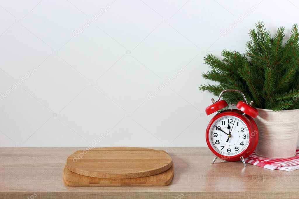 new Year's holiday background with an empty countertop an alarm clock and branches of a Christmas tree two cutting boards as a pedestal a countertop kitchen