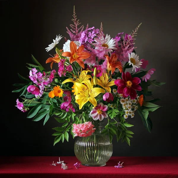 Bouquet from cultivated flowers in a jug on a red cloth — Stock Photo, Image