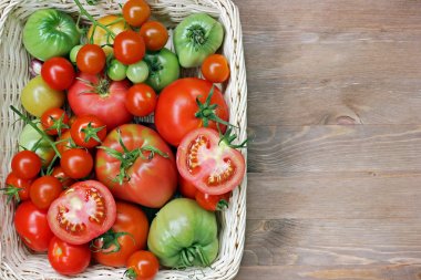 Fresh red and green tomatoes in a basket on a table clipart