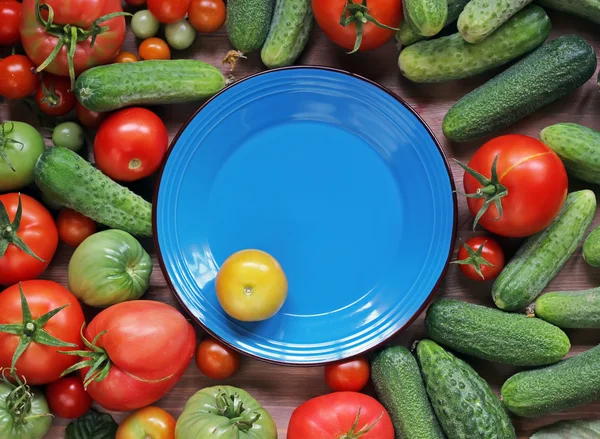 Tomates y pepinos se encuentran en una mesa con un plato azul en la c —  Fotos de Stock