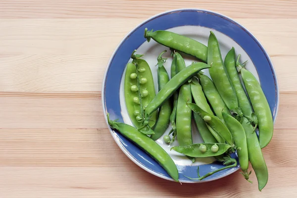 Peas pods on a plate with a blue border on a wooden table. — Stock Photo, Image
