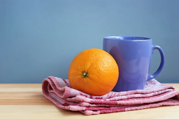 Xícara azul e laranja em uma toalha em uma mesa de madeira — Fotografia de Stock