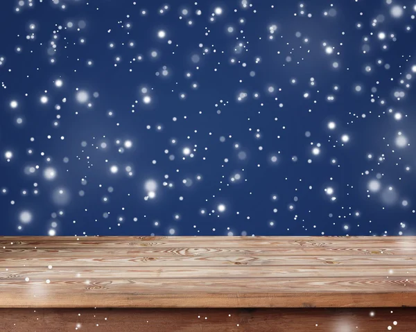 Leerer Holztisch auf blauem Hintergrund mit dem fallenden Schnee. — Stockfoto
