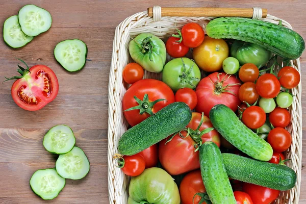 Los pepinos frescos, los tomates rojos y verdes sobre la mesa yacen en la cesta, la vista superior . — Foto de Stock