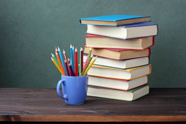 Yığın kitap renk kapsar ve bir fincan renkli kalemler.