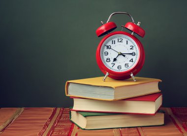 Üç kitap ve kırmızı bir çalar saat ile natürmort.