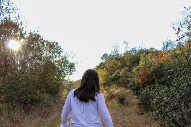 Genç esmer kız arka planda ağaçlarla ormanda poz veriyor.