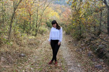 Genç esmer kız arka planda ağaçlarla ormanda poz veriyor.