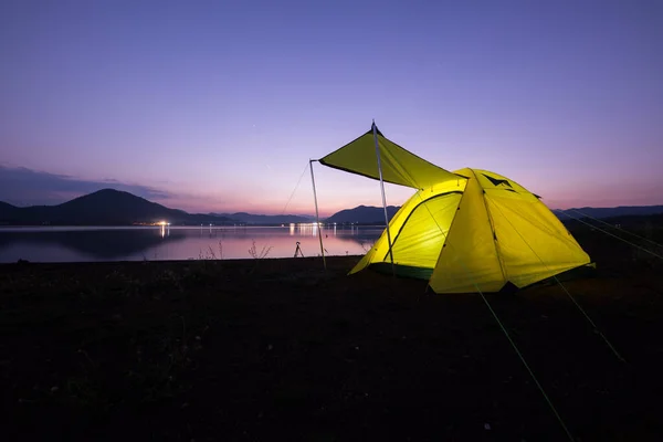 Gece vakti bulutlu gökyüzünün altındaki yeşil çim tarlasında çadır kurmak
