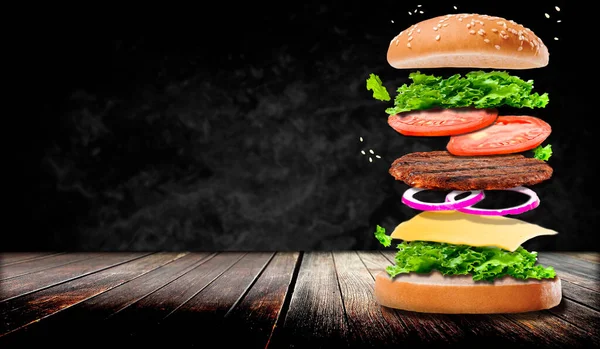 Karanlık bir arka planda köfte. Biftek, salata, domates, soğan, peynir dahil. Güzel, karanlık bir arka planda. Tahta bir masada hamburger.