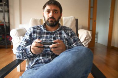 Genç bir adam elinde uzaktan kumandayla video oyunları oynamaya odaklanmış.