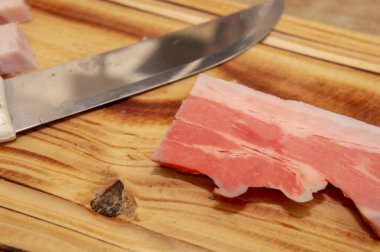 Tahta kesme tahtasının tepesine yerleştirilmiş parlak metal bıçağın yanında büyük bir dilim pastırma..