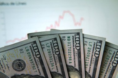 Filmin ön planında bir sürü 100 dolarlık banknot var. Arka planda bir borsa grafiği bulanık. Bir bilgisayar ekranının önünde çekilmiş.