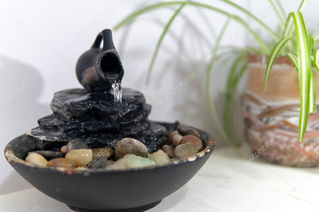 zen water fountian over a white background next to a green plant in a pot