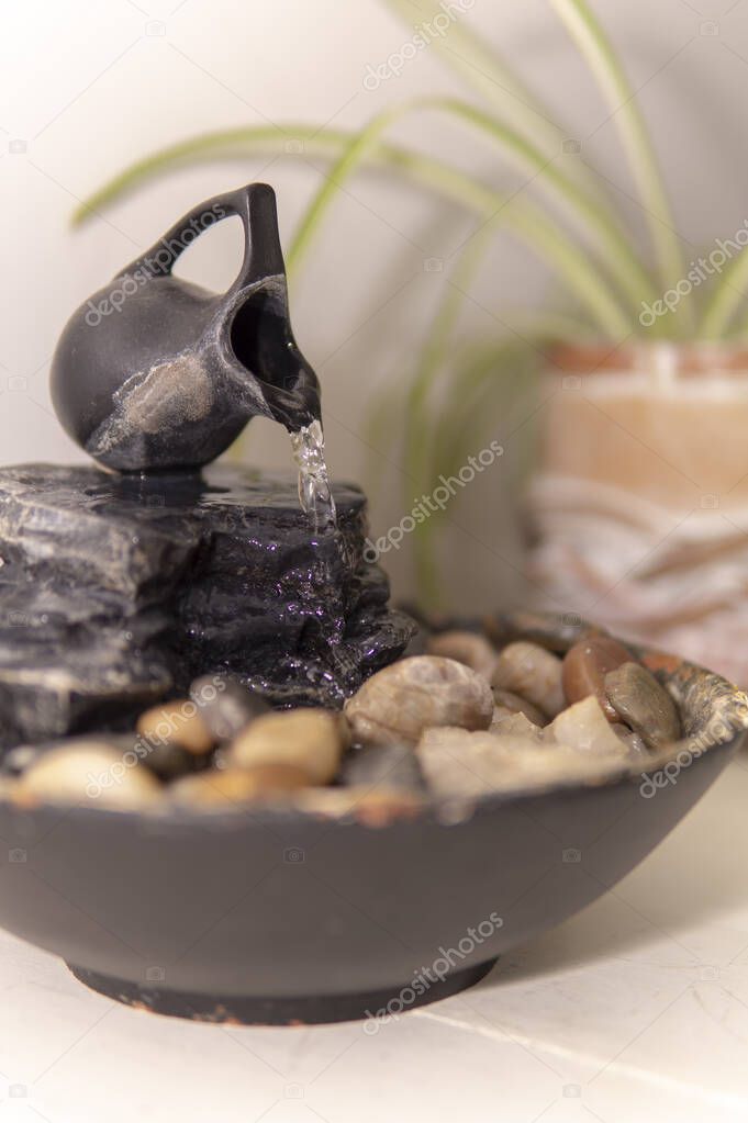 zen water fountian over a white background next to a green plant in a pot