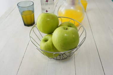 Beyaz ahşap bir masanın tepesindeki yeşil elma kasesinin yakın görüntüsü.