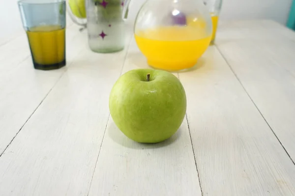 Beyaz ahşap bir masanın üzerindeki yeşil elmanın yakın görüntüsü