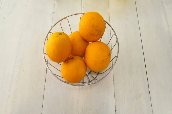 Oranges in a bowl. On top of a white wood table