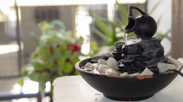 Sıcak bir yaz sabahı birkaç yeşil bitkinin yanındaki dekoratif bir zen çeşmesinin yakın görüntüsü.