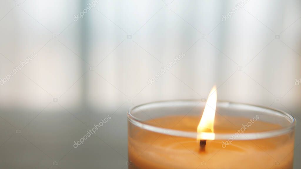 close view of lit candle with a textured white and gray blurred background