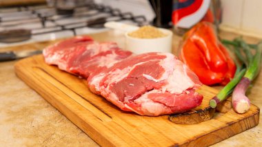 Tahta bir kesme tahtasının tepesinde büyük bir parça çiğ kırmızı etin yakın görüntüsü. Diğer bileşenlerle çevrili.