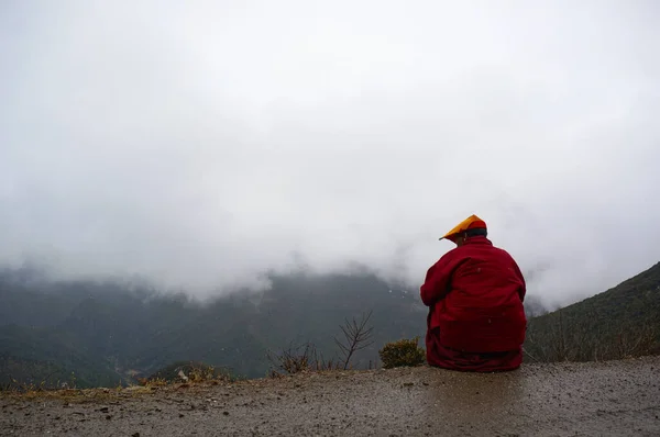 Kırmızı cüppeli Tibetli keşiş dağlarda yolda oturuyor.