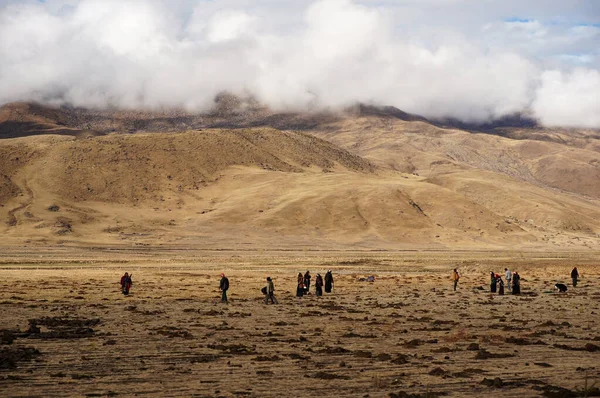 Koyu renk elbiseli insanlar sahada yürüyor. Sarı bozkır ve tepeler.