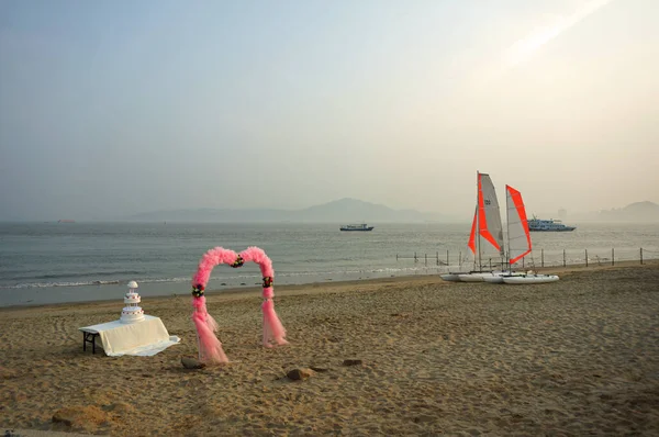 Pembe düğün kemeri ve boş bir sahilde beyaz pasta.