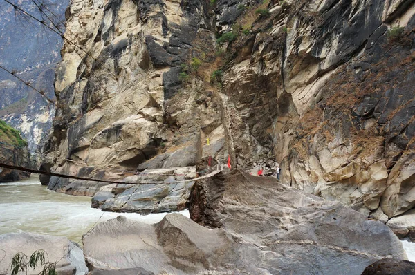 Dağ nehri üzerinde ip köprüsü. Devasa yüksek kaya oluşumu. Kahverengi uçurum duvarı