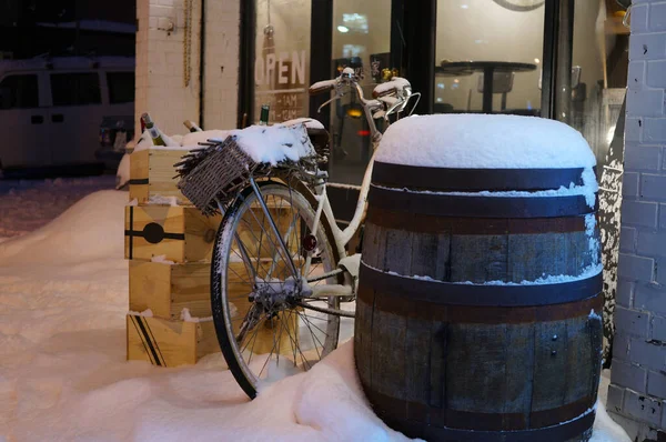 Ahşap şarap fıçısı, şarap kutuları ve cam kafenin kapısının yanında karla kaplı bisiklet.