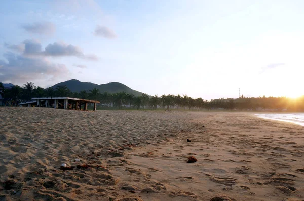 Boş kumsalda gün batımı. Arka planda palmiye ağaçları ve tepeler