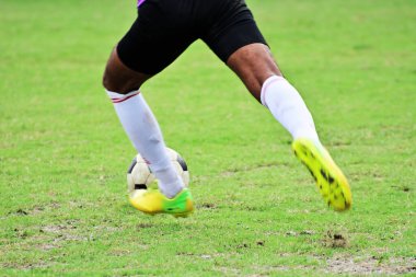 Futbol sahasında futbol topunu tekmelemek için koşan futbolcuların yakın çekimi.