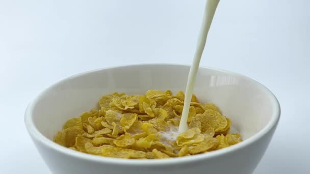ゆっくりとした動きでコーンフレークのボウルにミルクを注ぐ 白の背景に健康的なシリアル朝食 — ストック動画