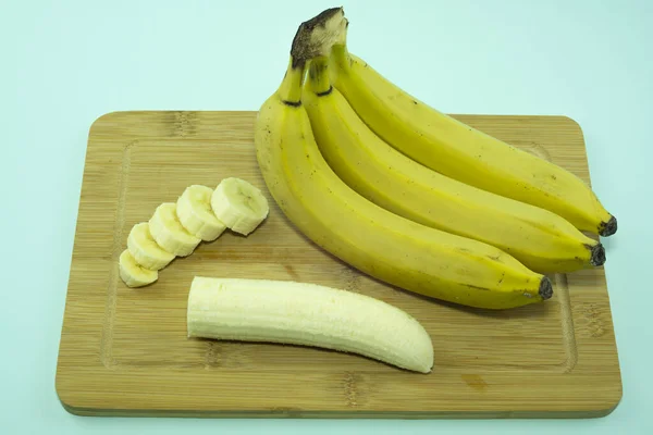 Banane pelée sur une planche à découper avec des morceaux hachés et une poignée de bananes entières. — Photo