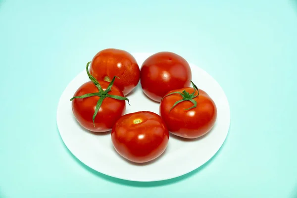 Cinq tomates rouges sur une assiette blanche isolée sur un fond bleu. — Photo
