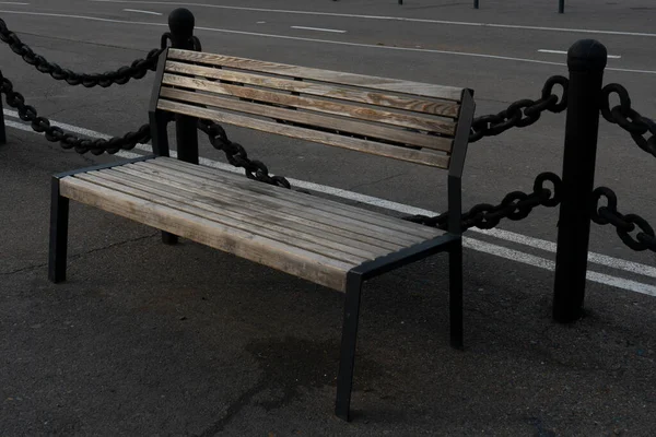 Wooden bench on the asphalt embankment fenced with pillars with massive chains. — Stock Photo, Image