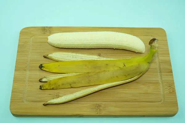 Очищенный банан на разделочной доске с банановой кожей. — стоковое фото
