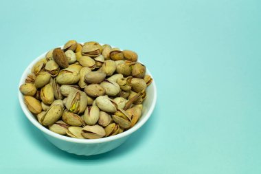 Mavi arka planda beyaz bardakta bir demet fıstık..