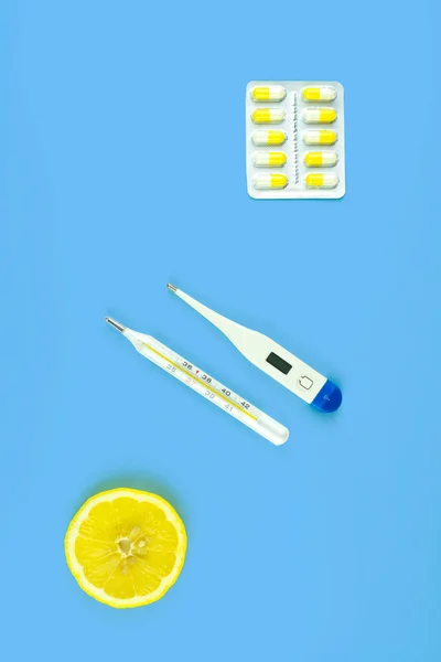 Dois termômetros, pílulas e uma fatia de limão em um fundo azul. — Fotografia de Stock