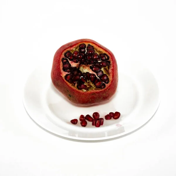 Гранат со спелыми красными ягодами на белой тарелке. — стоковое фото