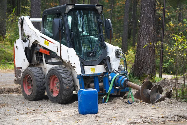 Compact tractor with drilling rig in the forest.
