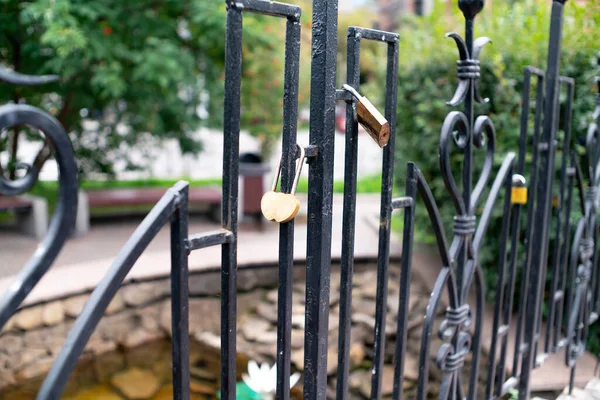 Curly black metal fence with padlocks. Brass locks in the shape of a heart. — Stock Photo, Image