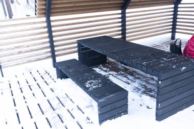 Çatının altındaki açık havada siyah ahşap bir bank ve masa..